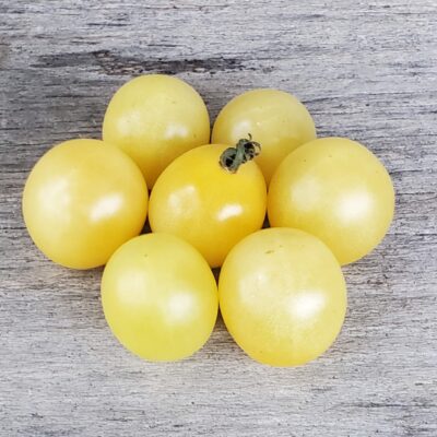 A cluster of seven yellow Tomato White Cherry tomatoes, of the heirloom variety, on a wooden surface.