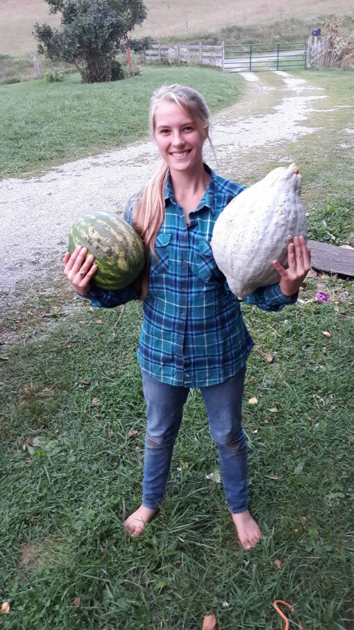 Lydia holding a watermelon alongside a huge Blue Hubbard Winter Squash.
