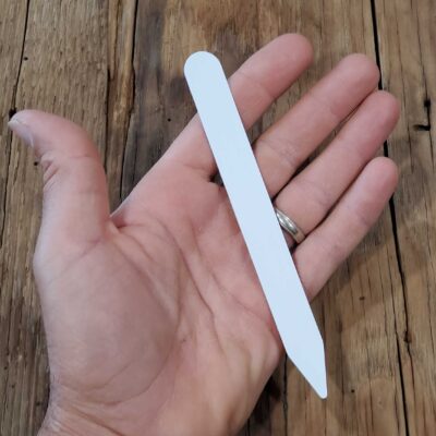 A hand holding a 6" Plastic Plant Marker Label on a wooden surface.