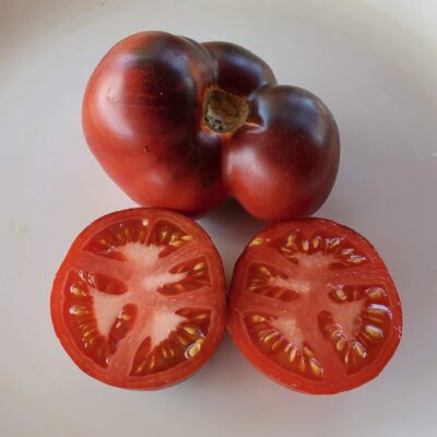 Sliced red, meaty Indigo Apple tomato with a whole tomato to the side.
