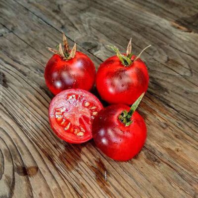 A Tomato Kaleidoscope Jewel set on a wooden surface, with one sliced open to reveal its juicy interior.