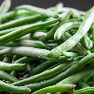 A close-up of a pile of fresh Bean Pole Old Homestead (Kentucky Wonder) beans on a dark surface.