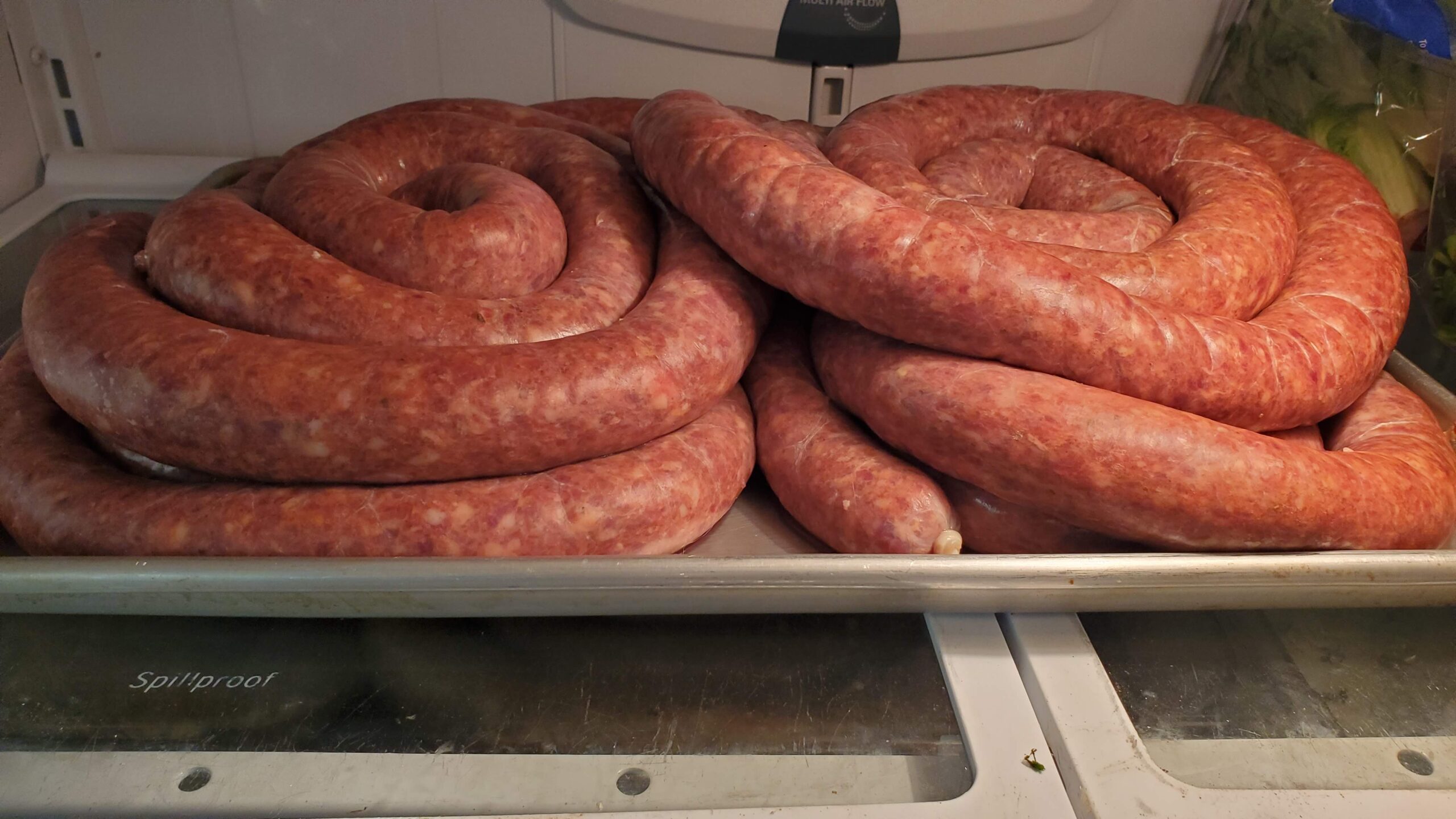Two large coils of raw sausage are arranged on a metal tray inside a refrigerator.